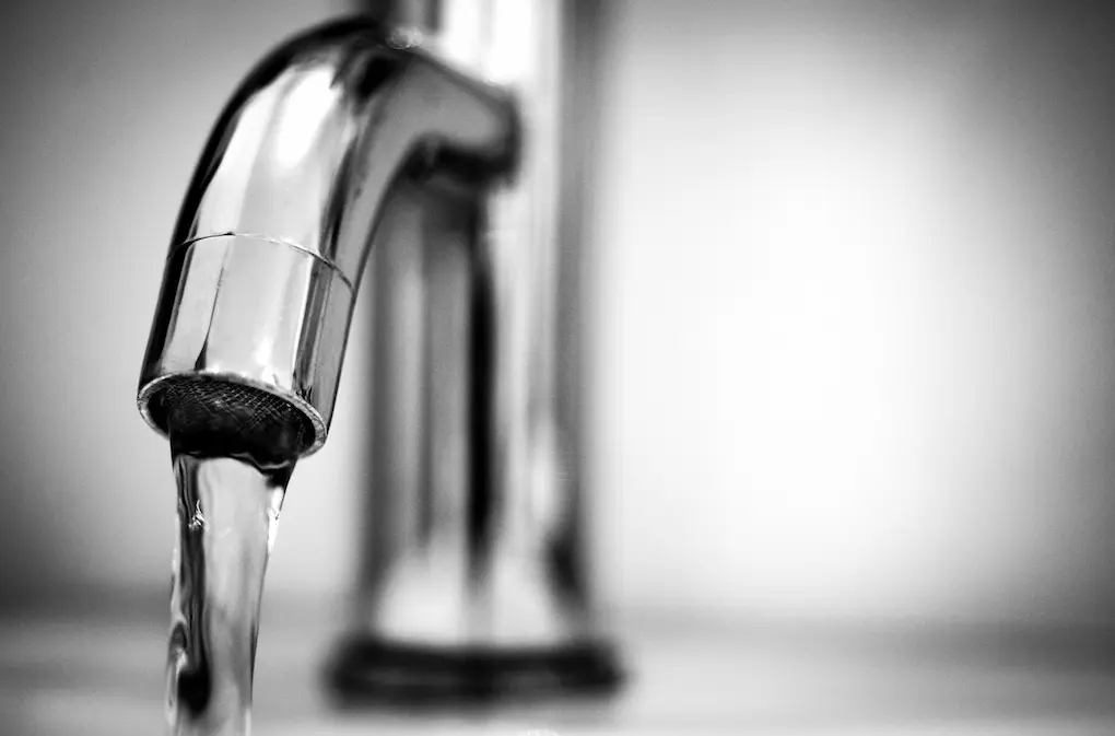 Picture of a sink with tap water running through the faucet for the article about toxic PFAS and forever chemicals in water.